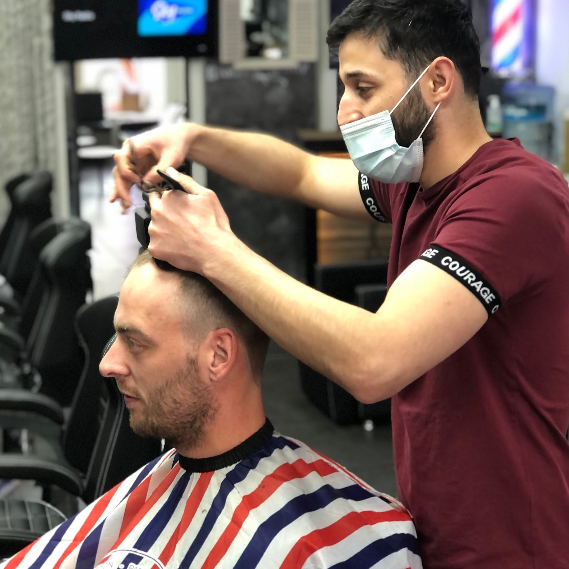 Een barbier aan het werk met tondeuse en kam, op de achtergrond een barbierspaal